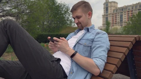 The young guy plays on the smartphone a game and smiles. Stock Footage 89448358
