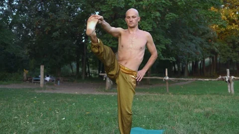 Young Guy Practicing Yoga Performs Asanas Standing on One Foot in the Park Stock Footage 85755329