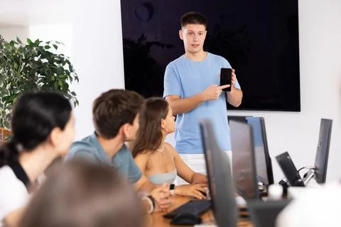 Young guy presenting educational mobile app to group of students 写真素材