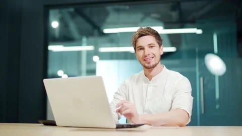 A young guy, a programmer or an entrepreneur behind a laptop, looks at the camer Stock Footage 229085606