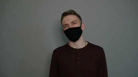 Young guy in a protective mask on a gray background. Shows hands. Hygiene Stock Footage 129023036