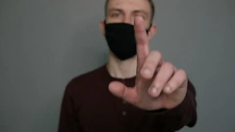 Young guy in a protective mask on a gray background. Shows a finger. Caution Stock Footage 129025416