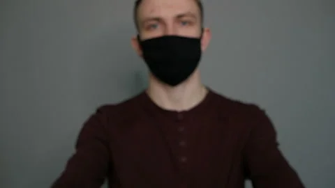 Young guy in a protective mask on a gray background. Shows hands. Hygiene Stock Footage 129027789