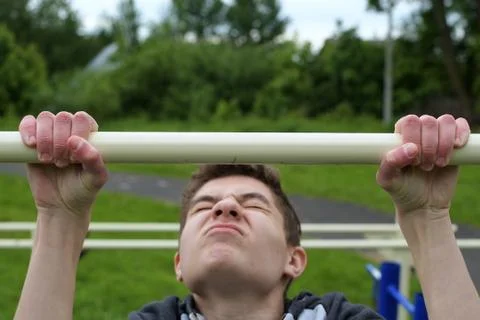 A young guy pulls himself up on a horizontal bar on a street training ground Stock Photos