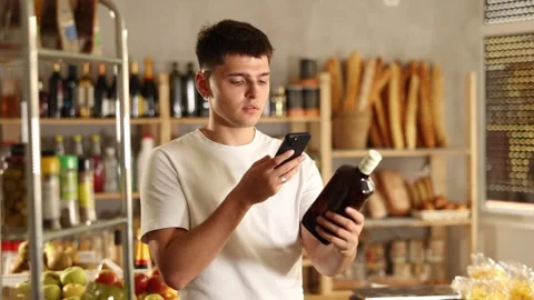 Young guy purchaser scanning with smartphone QR code label of bottle of whiskey Stock Footage 307066548