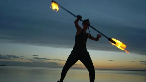 A young guy puts on a fire show against the backdrop of a sunset sky and a river 库存影片 194378897