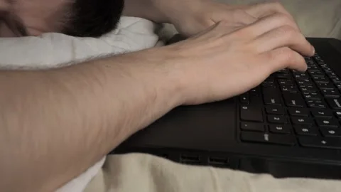 A young guy puts his head on the pillow, wearily knocks on keyboard Stock Footage 142754367