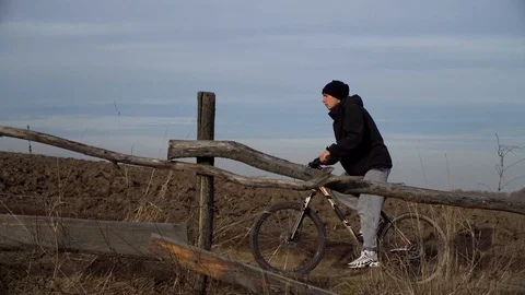 Young guy quickly climbs up on his bike.Male Riding Bike on dirt road Video stock 122237162