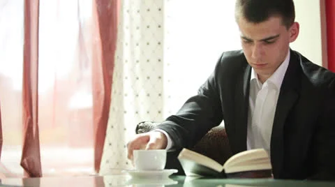 Young guy reading a book and drinking coffee Stock Footage 22769704