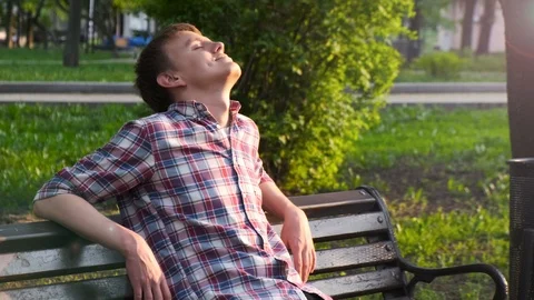 Young guy resting on a bench on a sunny day with his eyes closed 스톡 동영상 108380330