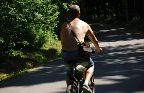 Young guy ride bikes without shirts in the summer in a tourist city. In the b Stock Photos