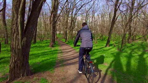 Young Guy Rides a Bicycle Along a Path in a Green Forest, Rear View in Slow Mo Stock Footage 182891790