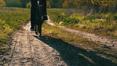 Young Guy Rides a Bicycle Along a Dusty Path in the Forest at Sunset Stock Footage 194680644