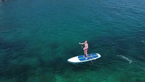 A young guy rides a SUP board on the turquoise coast of Koh Rok. Video stock 315843522