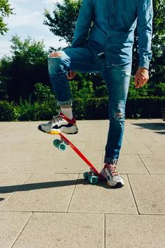 Young guy in ripped jeans standing with penny board in the park. summer Stock Photos