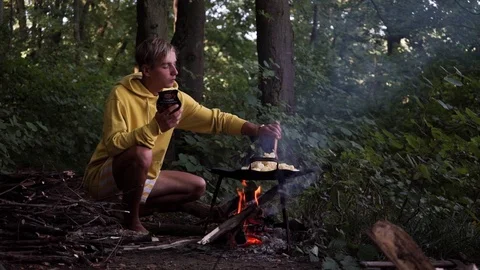 Young guy roasts potatoes over an open fire, mixes potatoes in a frying pan Stock Footage 114631272