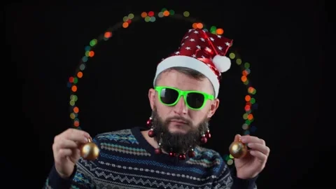 Young guy in a Santa Claus hat with toys on his beard with New Year's lights on Stock Footage 221278136