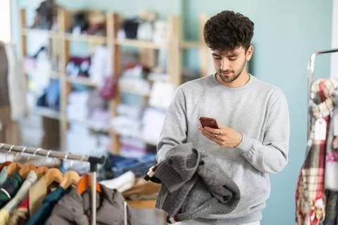 Young guy scanning QR-code on sweater in clothing store Stock Photos