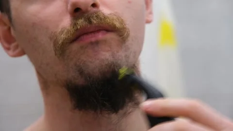 Young guy shaves his beard at home. Personal care. A man shaves his beard with Stock Footage 232632906