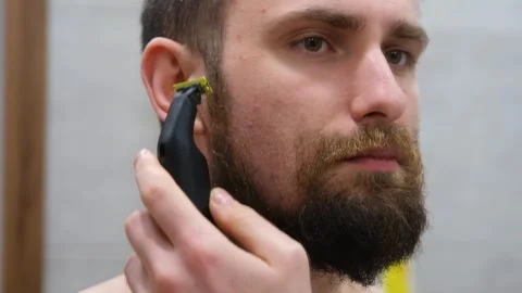 Young guy shaves his beard at home. Personal care. A man shaves his beard with Stock Footage 297718207
