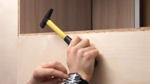 A young guy in a shirt hammers nails into plywood using a hammer. 库存影片 126317699