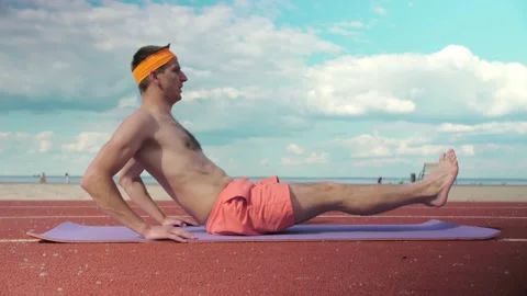 Young guy in shorts without a T-shirt does fitness exercises on the beach. Stock Footage 199252788