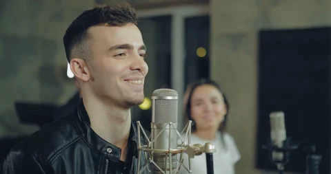 Young guy sings a song at the microphone. Musicians record a track in a 스톡 동영상 106963132
