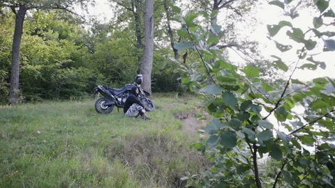 A young guy sits and rests next to his motorcycle on a cliff near the river 스톡 동영상 116413784