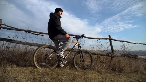 Young guy sits on a bicycle and looks at mountain landscape Stock Footage 122237146