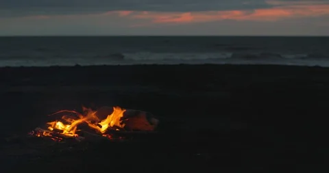 Young guy sits at the campfire on the beach. Young urban man near fire in the Video stock 123400169