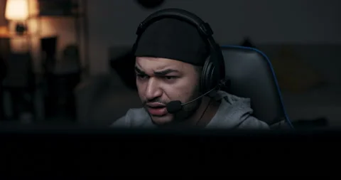 Young guy sits in dark room at computer desk. Player in the gray T-shirt has Stock Footage 214140487