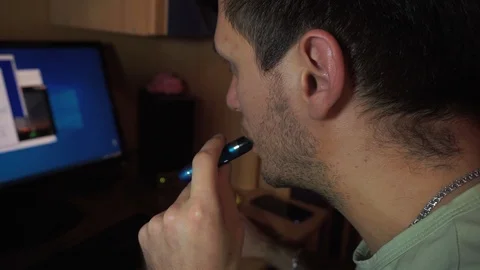 Young guy sits in front computer monitor with open windows, tabs, hovering vape Stock Footage 121537370