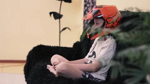 Young guy sits in a helmet on the couch and plays a console Stock Footage 198936374