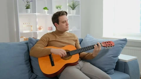 A young guy sits at home on the couch and plays the guitar. Stock Footage 170794651