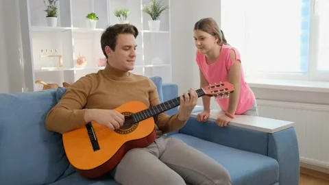 A young guy sits at home on the couch and plays guitar next to sister. Stock Footage 170795596