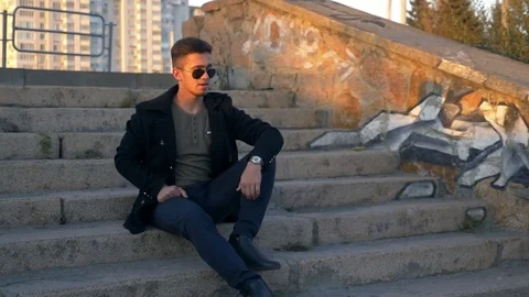 A young guy sits on the stone steps in the rays of a golden sunset 스톡 동영상 80986808