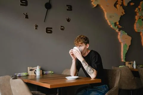 A young guy sits at a table in a coffee shop drinking coffee Stock Photos