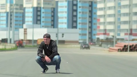 Young guy sits thoughtfully squatting down outdoors on a city street Stock Footage 138808806