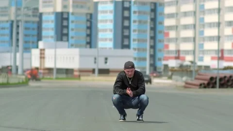 Young guy sits thoughtfully squatting down outdoors on a city street Stock Footage 138808811