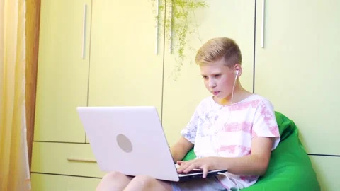 Young guy sitting on a bag chair, pear actively playing online game on laptop Stock Footage 138452958