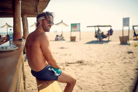 A young guy is sitting in the bar on the beach and enjoys the view. Summer,.. Stock Photos