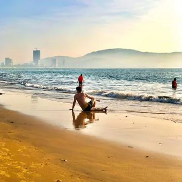 Young guy sitting on the beach and relaxing Stock Photos