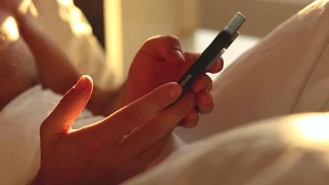 Young guy sitting at bed using smart phone at early morning Stock-Footage 343513089
