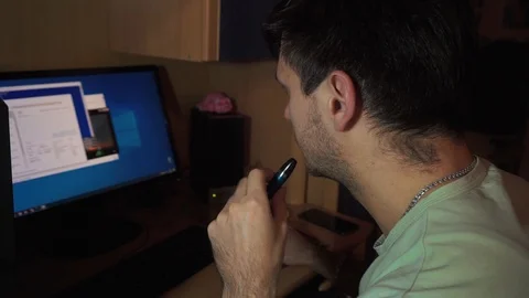Young guy sitting at computer, moves mouse window on monitor, hovering a vape Stock Footage 121537390