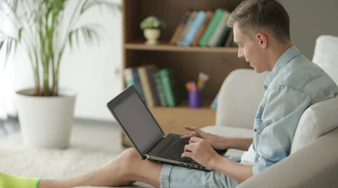 Young guy sitting on couch and using laptop Stock Footage 27691931