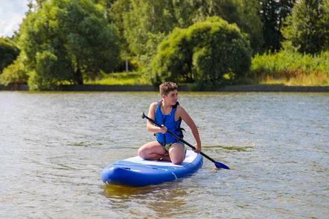 A young guy sitting down rides a SUP board, overcoming the waves with ease. Stock Photos