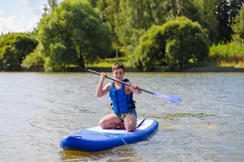 A young guy sitting down rides a SUP board, overcoming the waves with ease. Stock Photos