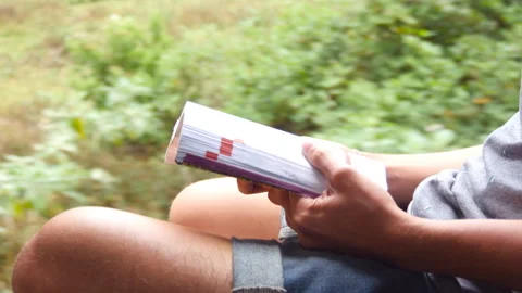 Young guy sitting near open door of moving train and reading interesting book Stock Footage 306126096
