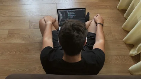 A young guy sitting in a room on the floor by the window uses a laptop. A Stock Footage 108773935