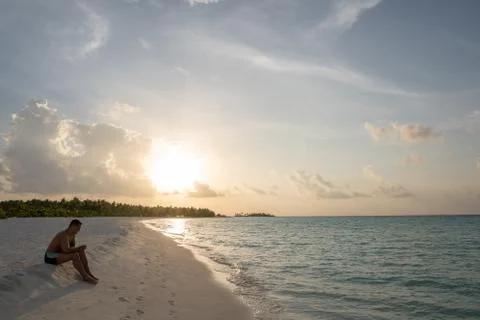 A young guy is sitting on a sandy beach and he is thinking about something. Foto stock